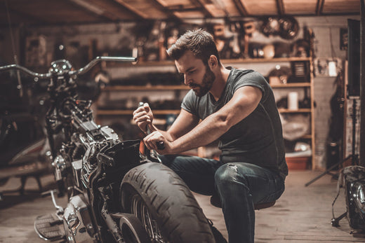 white bearded man kneeling down in a garage working on a motorcycle