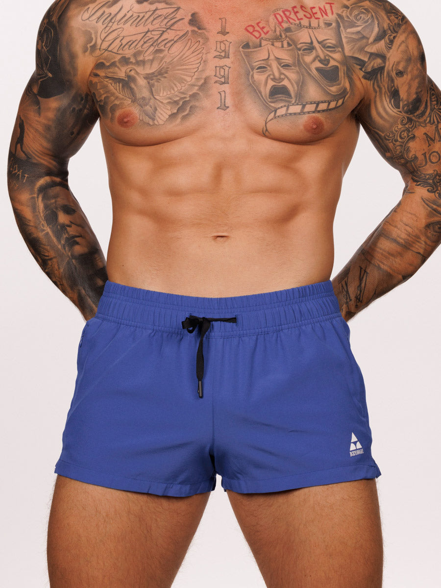 Front view of a male model wearing blue Body Aware square leg gym shorts 