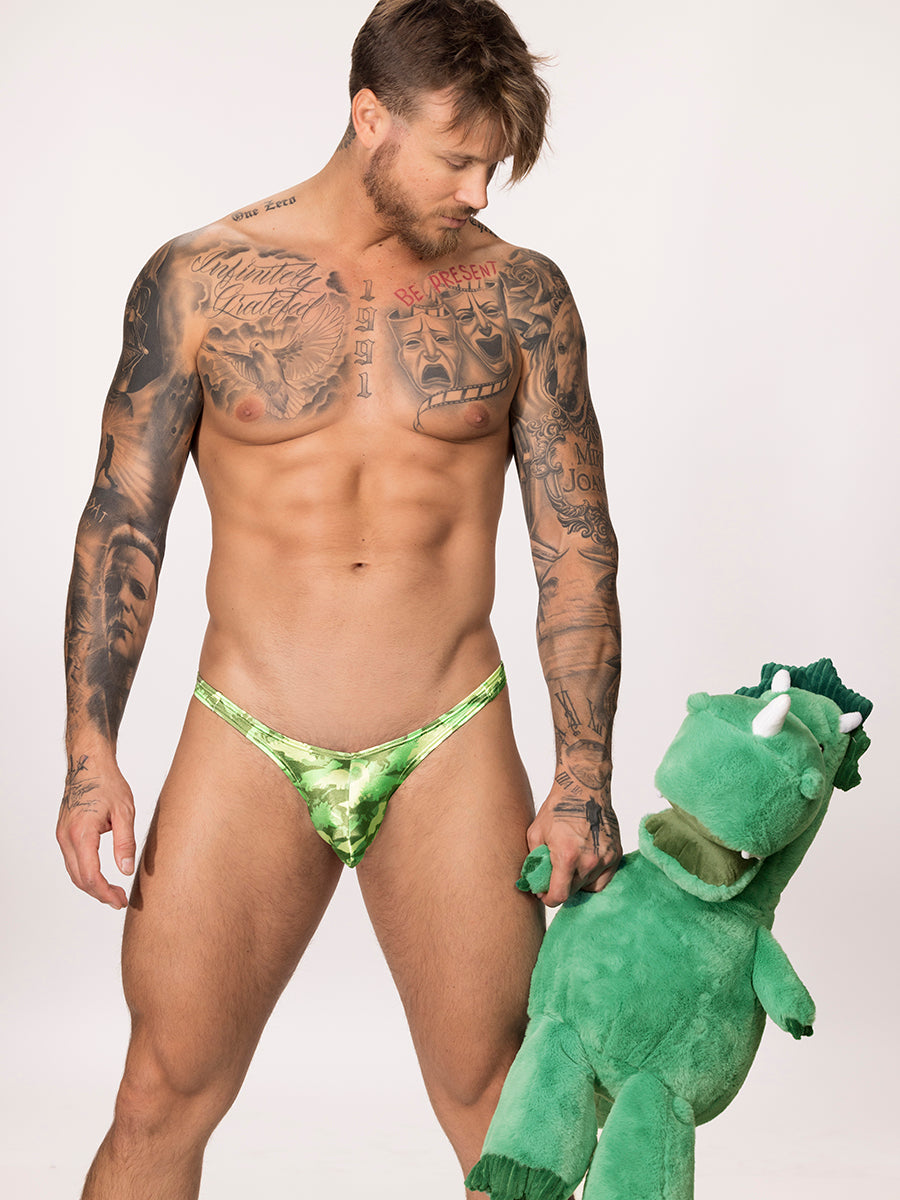 Front view of male model wearing a green satin Body Aware bikini brief while holding a dinosaur plushie 