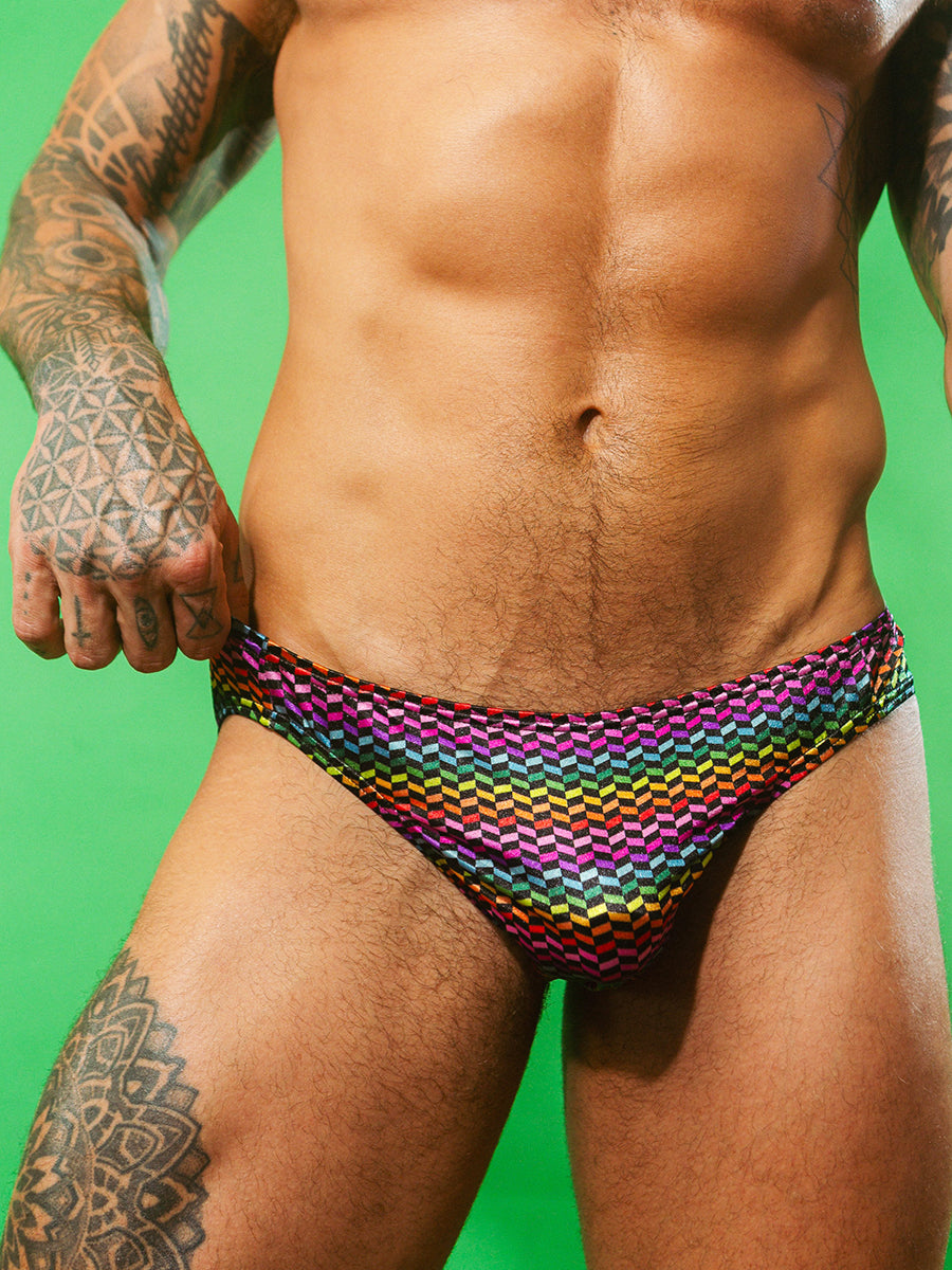 Closeup view of a man wearing a rainbow pattern satin brief against a green background.