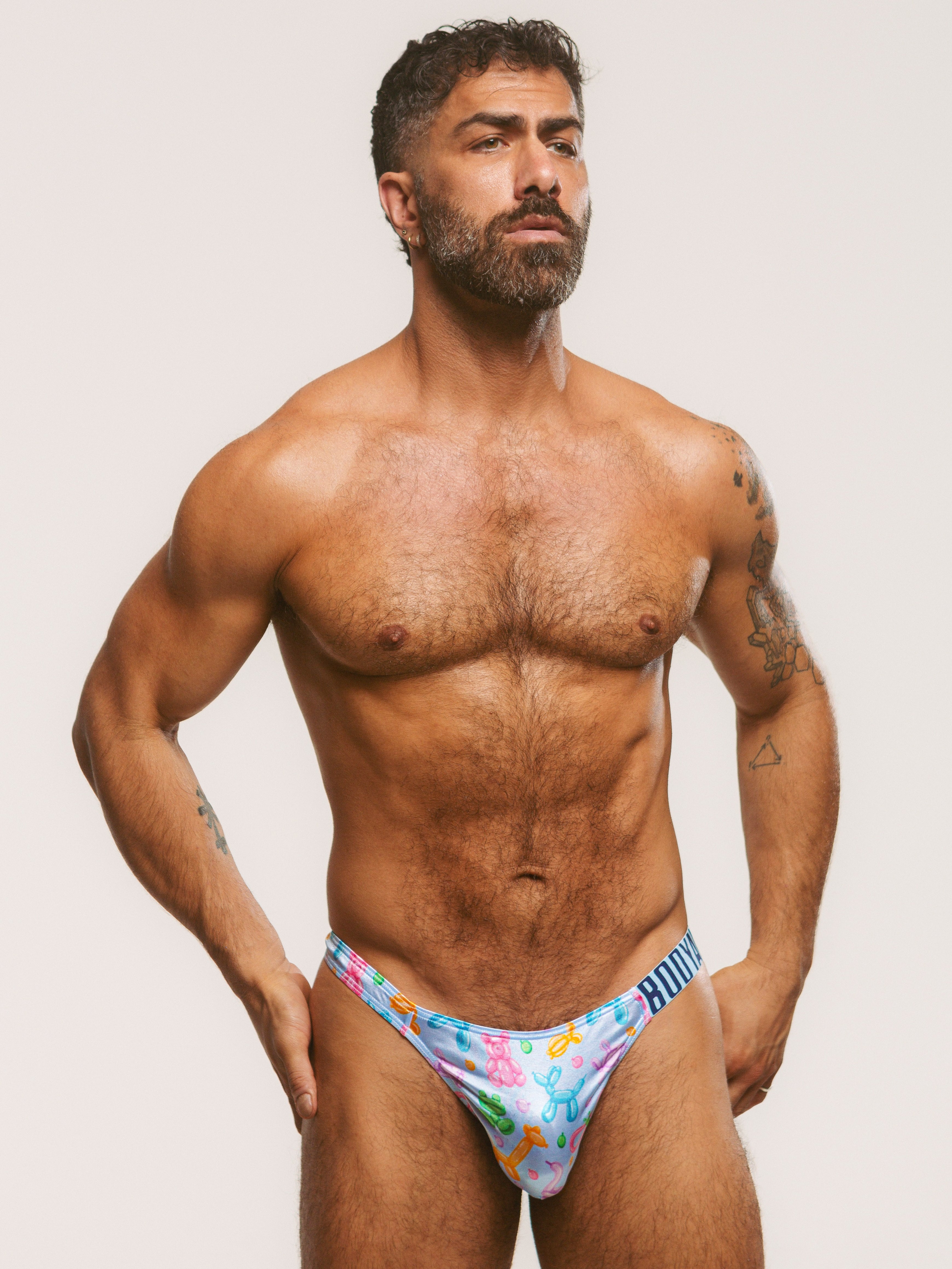 Front view of a man wearing a light blue satin thong with a Body Aware branded waistband.