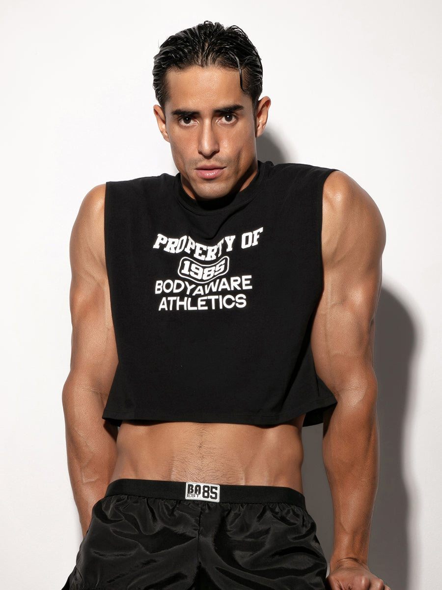 Man wearing a black sleeveless crop top with text, standing against a white background.