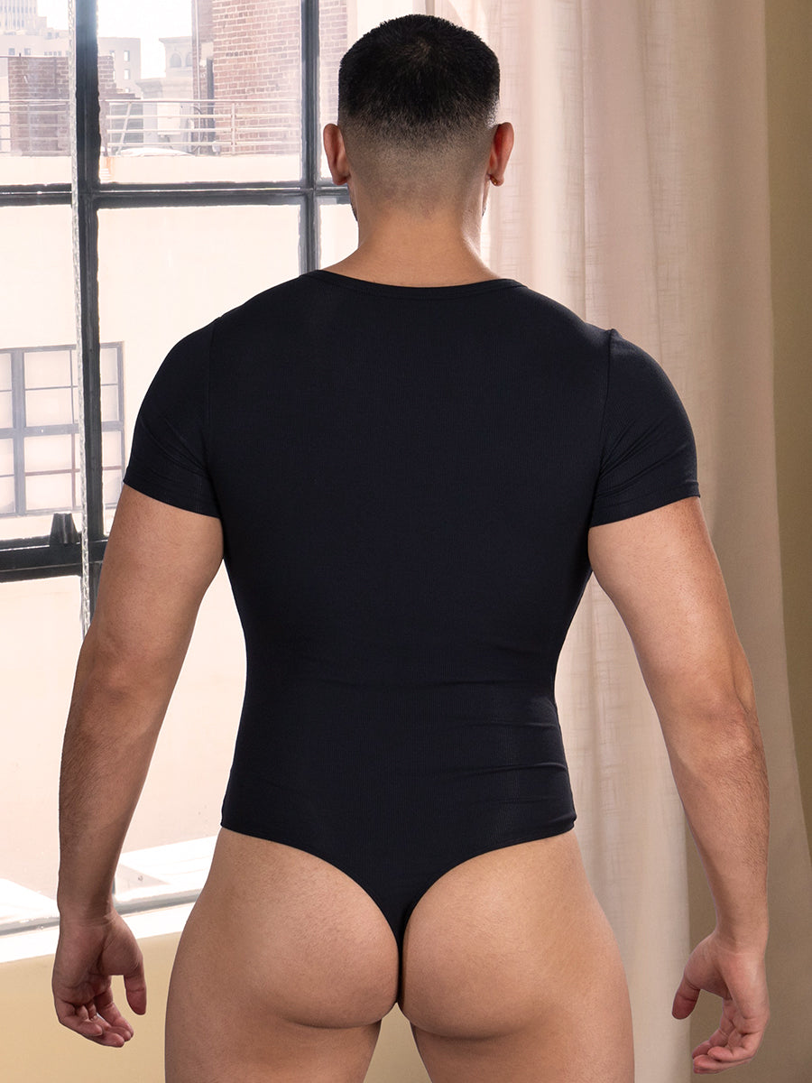Back view of a man wearing a black thong bodysuit standing in front of a window.