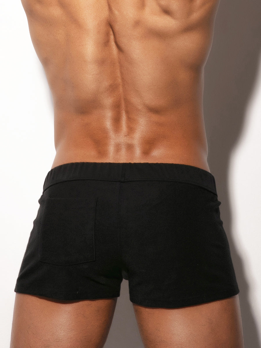 Man wearing black booty shorts against a neutral background