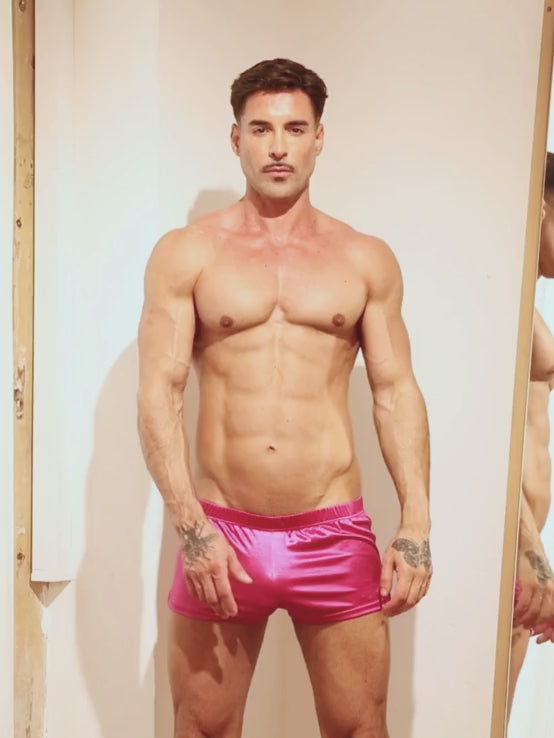 Video of a man wearing pink satin shorts, posing in front of a mirror.